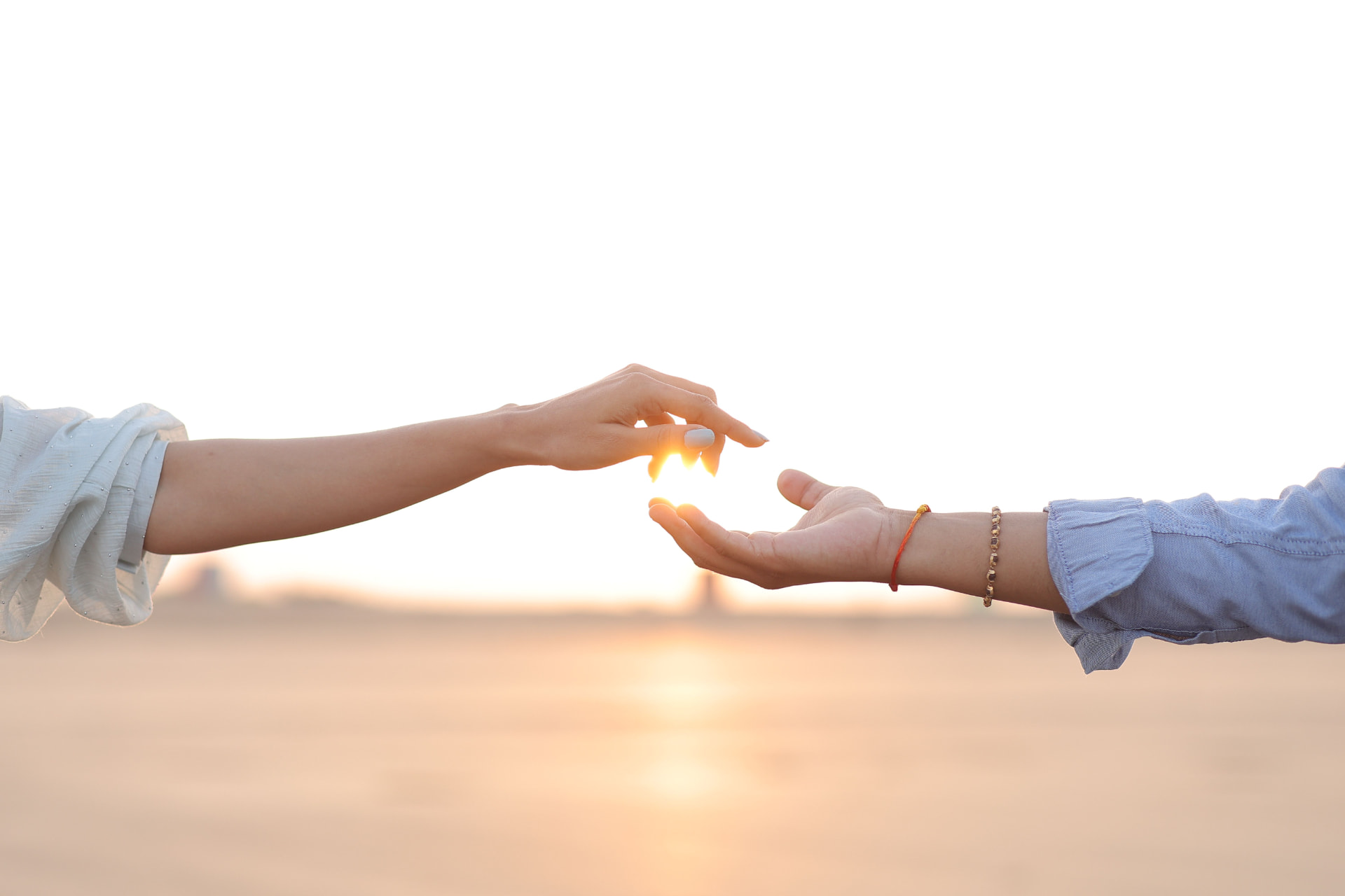 Two hands reaching toward one another at sunset, fingertips almost touching.