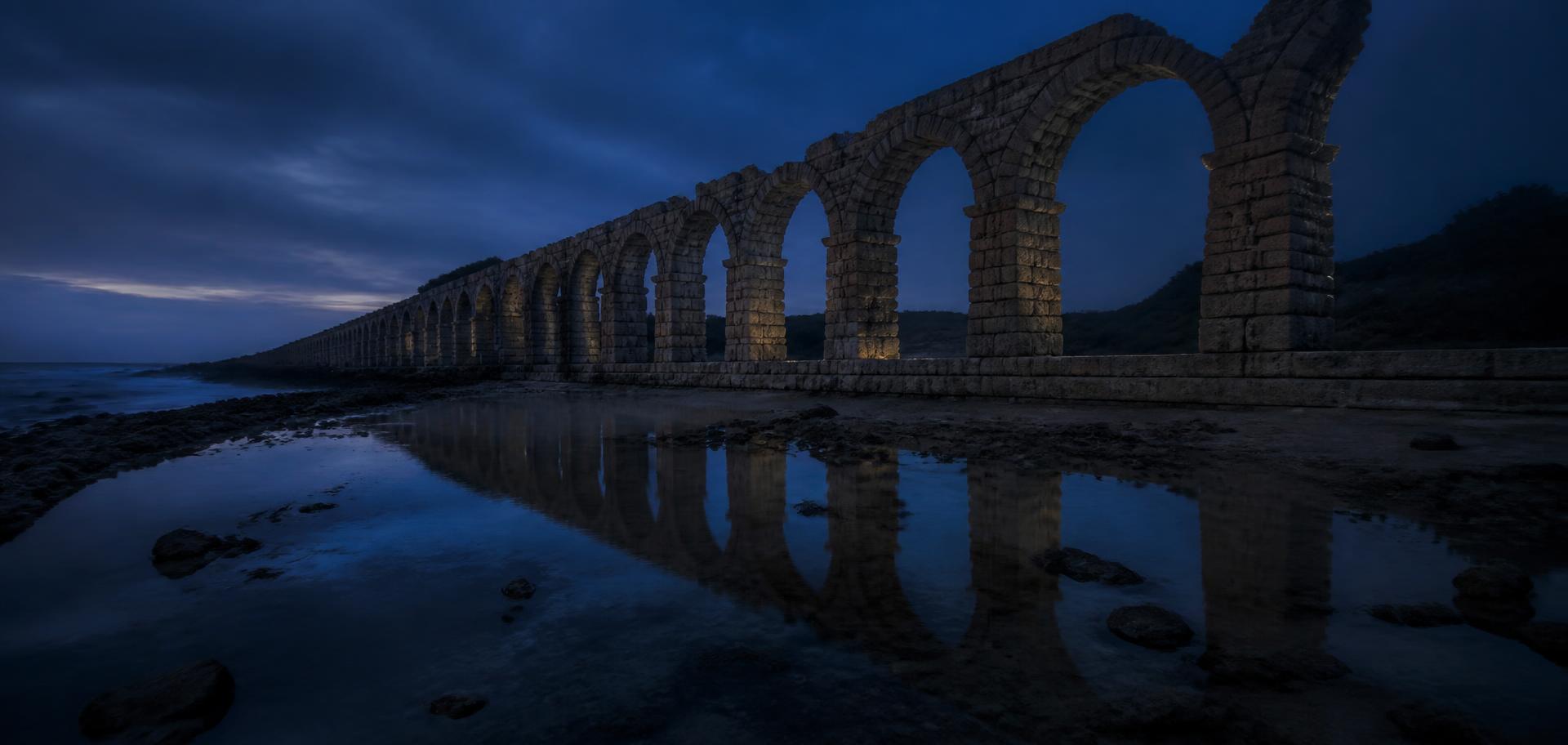 The aqueduct arcade at dusk beside still water